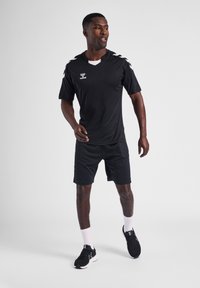 Zwarte sporttrui met witte accenten, korte mouwen en een V-halsontwerp. Gecombineerd met zwarte shorts en sportschoenen. Zachte stofstructuur.