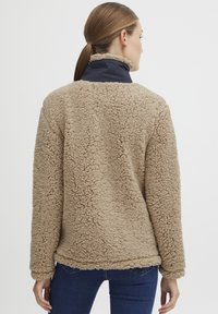 Veste en polaire beige avec un extérieur doux et texturé, dotée d'un col montant en marine et d'une coupe décontractée, conçue pour le confort.