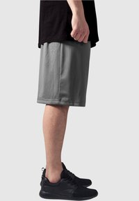 Grå atletiske shorts med en teksturert finish, som når til knærne, sammen med svarte joggesko. Toppdelen er en svart skjorte, delvis stukket inn.