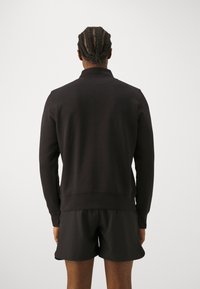 Sudadera negra con un cuello alto, puños y banda en la cintura acanalados. Combinada con pantalones cortos negros a juego. Tejido liso, de color sólido y sin adornos.