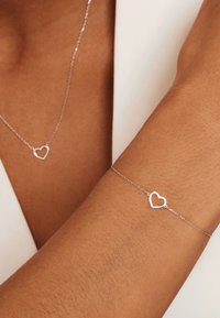 Zilveren hartvormige ketting en armband met delicate kettingen, voorzien van open hartaccents en een gladde, gepolijste afwerking.
