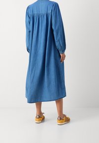 Denimkjole med lange ballonærmer, rygsøjle, samlingdetaljer og en afslappet pasform, suppleret af brune sneakers med hvide såler.