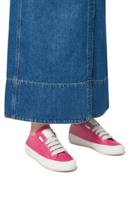 Pink low-top sneakers with white rubber soles and laces, featuring a smooth texture and understated branding. Worn with a blue denim skirt.
