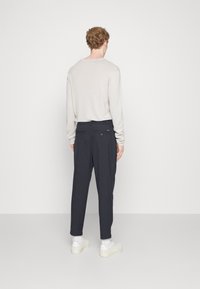 Light grey long-sleeve shirt and dark navy trousers with a relaxed fit, featuring dual back pockets and a plain texture. White sneakers complete the look.