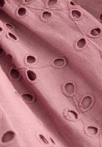 Rosa Stoff mit aufwendiger Bestickung, der kreisförmige Ausschnitte und dekorative Nähte zeigt. Weiche Textur mit einem zarten Design.