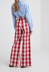 Punatut ja valkoiset ruudulliset korkeavyötäröiset laajat housut, joissa on sileä pinta, yhdistettynä vaaleansineään pitkähihamaiseen paitaan.