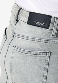 Jean en denim gris clair avec une poche arrière et une étiquette en cuir noire cousue au-dessus de la poche indiquant NOISY MAY.