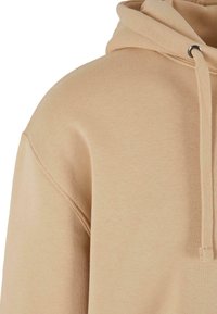 Felpa in cotone beige con finitura testurizzata, dotata di cappuccio con cordino e occhielli in metallo. Il design presenta una vestibilità comoda e orlo a coste.