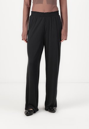 Black, wide-leg trousers with an elastic waistband; smooth texture and lightweight fabric. Worn with black slip-on shoes featuring silver accents.