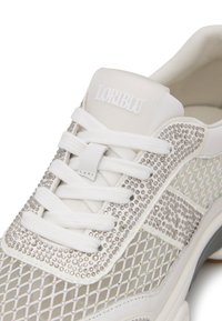 Sneaker bianco con tomaia in rete, adornato con strass trasparenti. Presenta lacci bianchi piatti, un tacco solido e un logo discreto sulla linguetta.