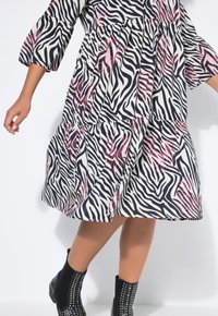 Vestido de estampado de cebra en blanco y negro con detalles en rosa, diseño en capas, mangas tres cuartos, combinado con botines negros con tachuelas.