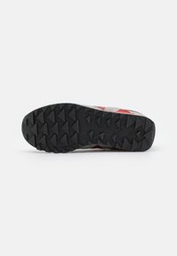 Scarpa sportiva grigia e rossa con suola in gomma nera testurizzata, caratterizzata da tasselli triangolari e un tallone rinforzato per una migliore aderenza e durabilità.
