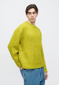 Kootud roheline kampsun tekstureeritud viimistlusega, ümmarguse kaeluse ja pikkade varrukatega, kombineeritud helesiniste teksapükstega. Lihtne, vabaaja disain.