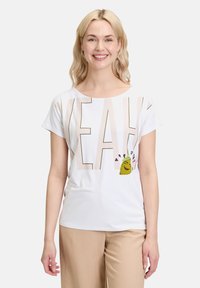 Witte t-shirt met korte mouwen waarop het woord "YEAH" in grote beige letters staat en een cartoon taco afbeelding met harten aan de linkerkant.