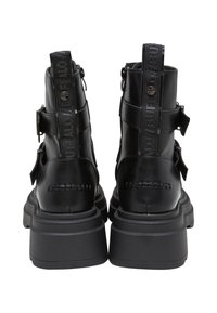 Botines negros con un acabado de cuero suave, suelas gruesas, correas ajustables y una pestaña en la parte trasera.