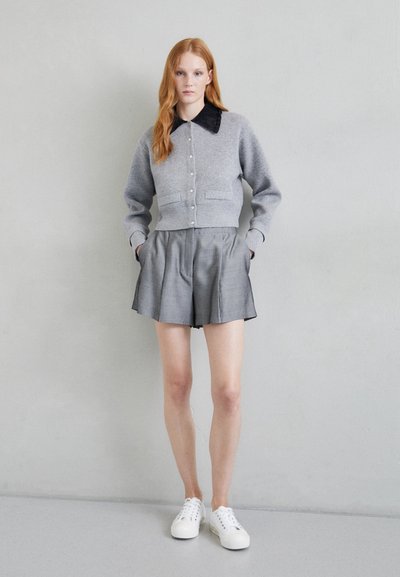 Pilka trumpa megztinis su juodu apykakle ir mygtukais, derinamas su pilkais raukiniais šortais. Bianchi sportbačiai užbaigia aprangą.