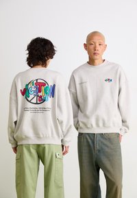 Gray sweatshirt with a colorful "VACATION CLUB" graphic on the back. Features dropped shoulders and a relaxed fit, complemented by beige pants.