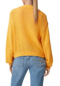 Yliuurrettu neulepaita kirkkaan keltaisena, jossa on löysä kudonta ja ribbireuna. Yhdistetty vaaleansinisiin farkkuihin, joissa on yksityiskohtia takana.