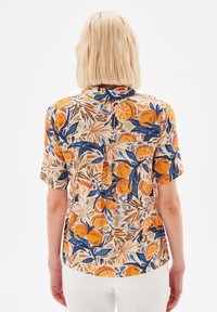Short-sleeve shirt in light fabric, featuring a vibrant orange and blue floral pattern on a beige background. Back pleat detail noted.