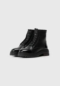 Botas de tobillo de cuero negro con un acabado brillante, acentos de volantes texturizados a lo largo de los lados y una suela de goma gruesa.