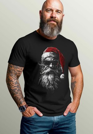 Black t-shirt featuring a detailed Santa graphic with sunglasses, a red hat, and a white beard. Model has tattoos and a watch, standing casually.