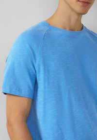 Lichtblauwe crew neck t-shirt met korte mouwen, gemaakt van gestructureerde stof. Beschikt over een subtiele gemarmerde print en een geribbelde halslijn.