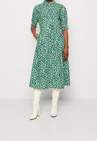 Zielona sukienka w kwiaty z kołnierzykiem zapinanym na guziki, wcięciem w talii i zwiewnym dołem. Stylizowana z białymi kozakami na słupku sięgającymi do kolan.