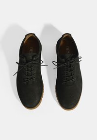 Zwarte veterschoenen met een geperforeerd ontwerp en platte rubberen zolen. Hete textuur met een contrasterende lichtbruine buitenzool.