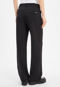 Black tailored trousers with a smooth fabric, featuring a single back pocket and a straight leg design. Finished with subtle hardware detail.