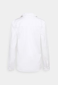 Camicia bianca a maniche lunghe con colletto classico, polsini con bottone e una texture liscia. Presenta uno yoke sul retro e una vestibilità dritta.