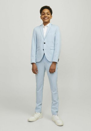 Traje azul claro con chaqueta de un solo botón, solapas con muesca y dos bolsillos, combinado con pantalones a juego y zapatillas blancas.