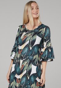 Kleid mit weitem Ärmel, das ein lebhaftes Blattmuster in Grün, Blau und Rot auf weißem Hintergrund zeigt. Glatte Stoffqualität mit Rundhalsausschnitt.