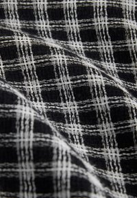Tissu noir texturé avec des fils blancs entrecroisés formant un motif en grille, montré en plis doux mettant en valeur son détail tissé.