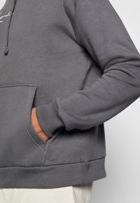 Felpa grigia con tasca a marsupio, polsini e orlo a coste. Realizzata in materiale morbido con una texture liscia e dotata di cappuccio con coulisse regolabile.