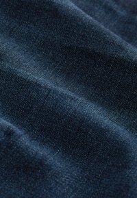 Close-up of dark blue denim fabric with visible texture and subtle folds creating soft shadows.