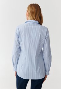 Chemise à manches longues bleu clair et blanche rayée, avec un col pointu, un ourlet arrondi et des poignets à boutons, fabriquée à partir d'un tissu lisse.