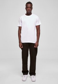 Fehér pamut póló sötétbarna nadrággal és fehér sportcipővel párosítva. Egyszerű dizájn, kerek nyakú és egyenes szabású. Nincsenek minták vagy díszítések.