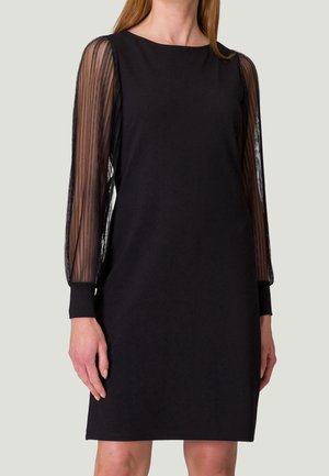 Robe noire jusqu'aux genoux avec manches longues transparentes plissées et poignets unis portée par une personne aux longs cheveux.
