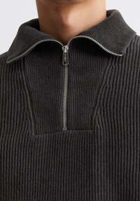 Dunkelgrauer, gerippter Pullover mit Reißverschluss am Kragen. Verfügt über ein strukturiertes Muster und einen Frontreißverschluss. Hochgeschlossener Kragen für einen bequemen Sitz.
