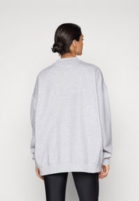 Sudadera grande gris con cuello redondo y mangas largas. Textura suave y puños acanalados, llevada sobre leggings negros.