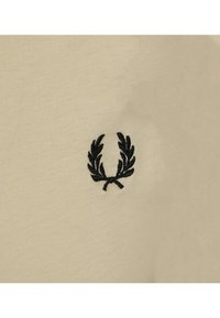 Tela de algodón beige con una textura suave que presenta un pequeño logotipo de una corona de laurel negra bordada en el centro.