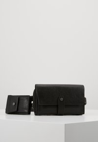 Svart texturerad läder crossbody-väska med viklock, magnetknäppning och avtagbar rem. Kompakt design för mångsidig användning.