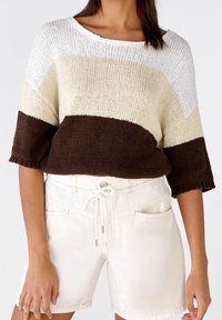 Suéter de punto con rayas horizontales en blanco, crema y marrón; escote ancho, mangas cortas y dobladillo ribeteado. Combinado con pantalones cortos de mezclilla blancos.