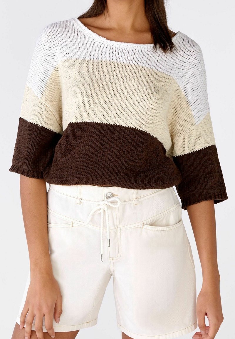 Suéter de punto con rayas horizontales en blanco, crema y marrón; escote ancho, mangas cortas y dobladillo ribeteado. Combinado con pantalones cortos de mezclilla blancos.