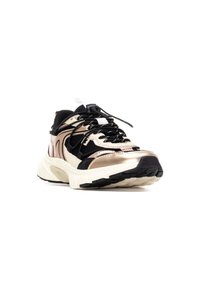 Zapatilla negra, dorada y crema con un upper texturizado, que presenta paneles de malla, cordones en contraste y una suela de goma gruesa con surcos de tracción.