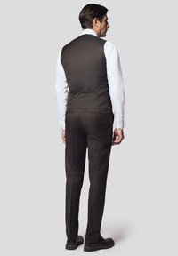 Brązowa kamizelka w wzór jodełkowy z tylnym wiązaniem, zestawiona z brązowymi spodniami w kratę. Pod spodem znajduje się biała koszula oraz ciemne buty.