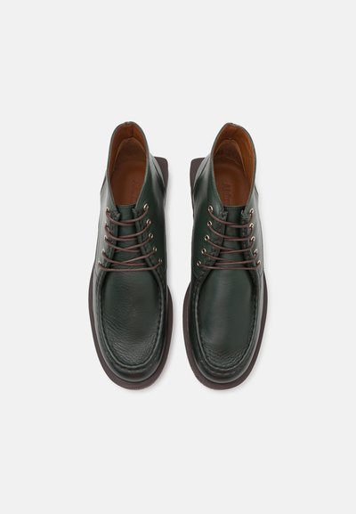 Green leather shoes with a rounded toe, brown accents, and six eyelets. Features a textured surface and a contrasting dark sole.