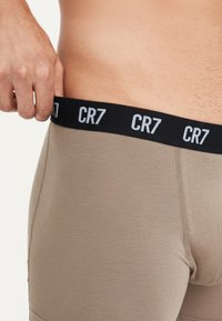 Beige boxer briefs with a black waistband featuring "CR7" logo in white. Smooth texture, fitted shape, showing waistband grip.
