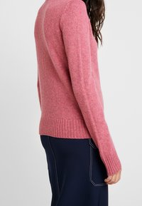 Maglione rosa lavorato a maglia con polsini e orlo a coste, dalla texture morbida e vestibilità leggermente ampia, mostrato da un angolo laterale.