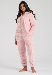Roze fluffy onesie met een capuchon. Zachte textuur, met berenpatronen. Opgerolde mouwen en enkels, twee voorzakken. Gezellig ontwerp.